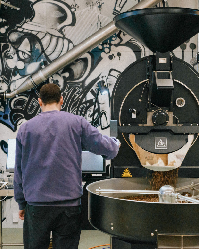 Person operating a coffee roasting machine with a colorful mural in the background